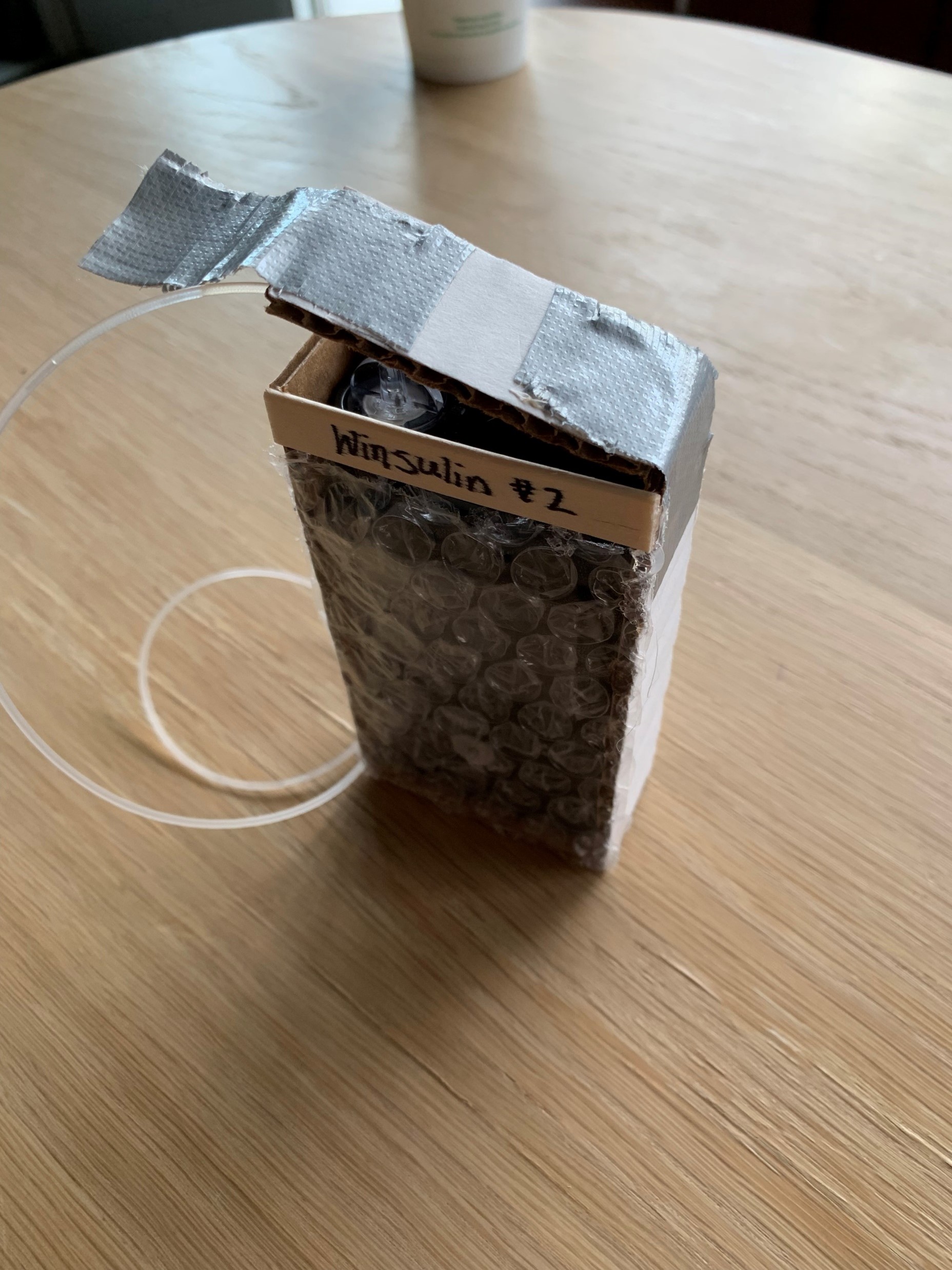 a cardboard prototype of an insulin pump holder with rubber tubing coming out the top