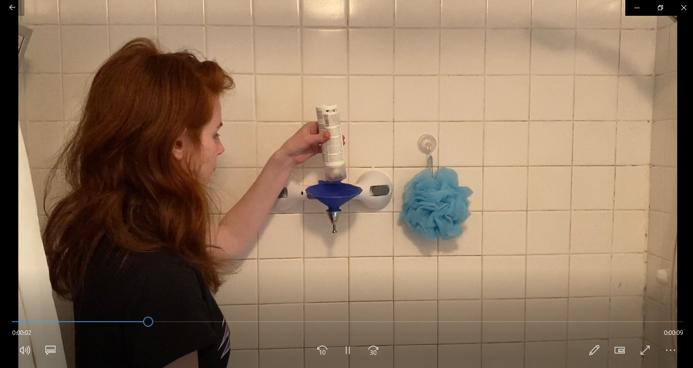 a person squeezing liquid from a bottle into a funnel mounted on a bathroom wall